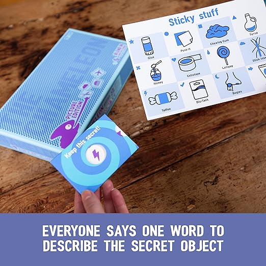 Hand holds a blue secret card beside a blue game box and a category sheet with icons of sticky items on a wood table.