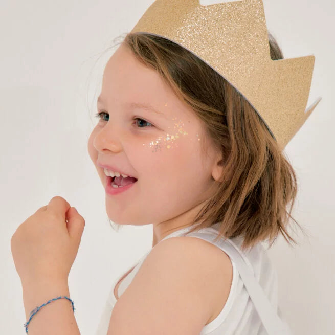 A smiling child wearing a shimmering gold glitter crown with pointed peaks.