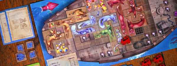 Ship-shaped game board with colorful cat polyominoes, cards, and red meeples on a wooden table.