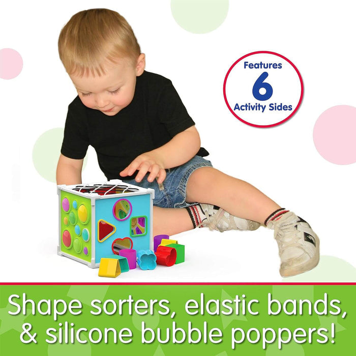 Toddler playing with a blue activity cube featuring colorful bubble poppers, shape sorters, and elastic bands.