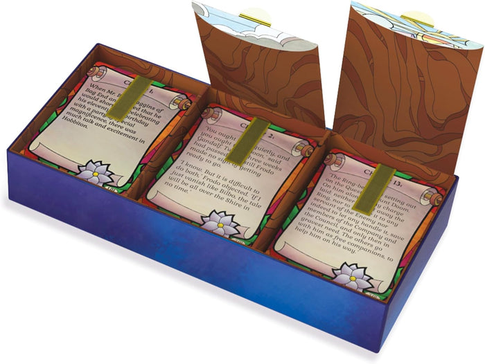 Open purple game box with three compartments holding cards with scroll illustrations and green ribbon pull-tabs.