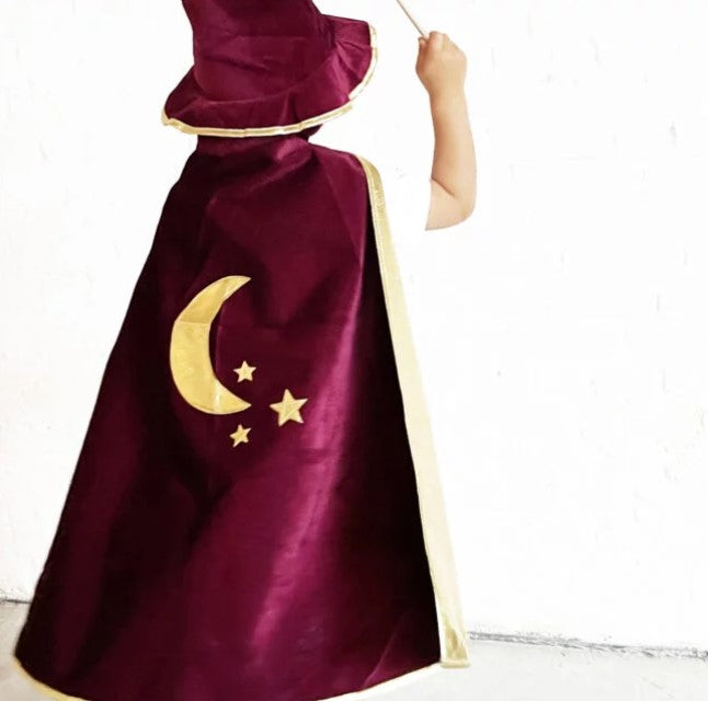 Child in a bordeaux velvet magician's cape and matching pointy hat with gold moon and star accents.