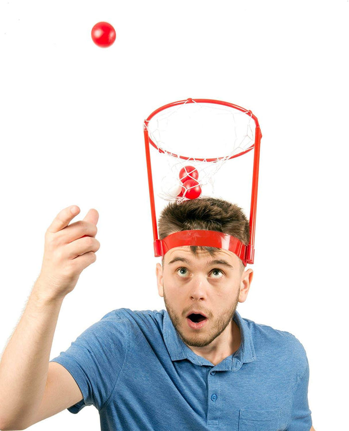 Man wearing a red plastic head-mounted basketball hoop catching small red balls in a white net.
