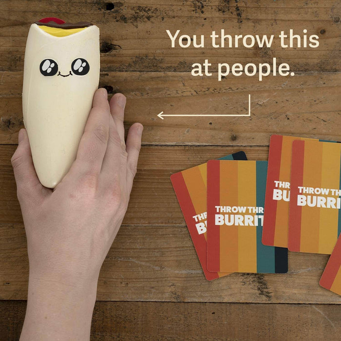 Hand holding a squishy white burrito toy with a cute face next to colorful game cards on a wooden table.