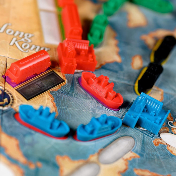 Close-up of red, blue, and green plastic train and ship pieces on a detailed sea and land board game map.