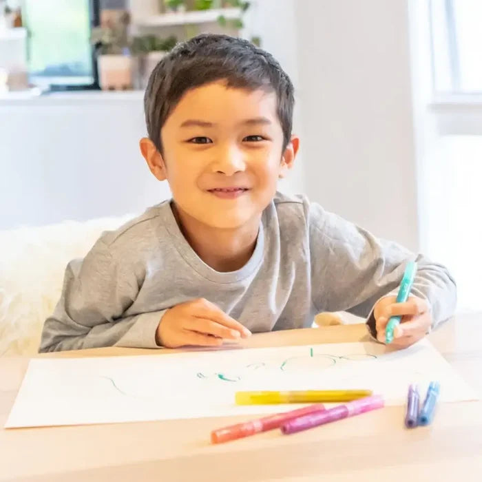 Smiling boy drawing on paper with colorful, sparkling markers in shades of pink, yellow, blue, and purple.