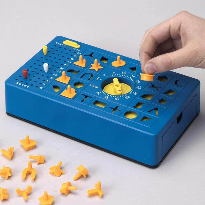 Blue rectangular game board with yellow shaped pieces, a central timer dial, and a hand inserting a round piece.