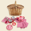 Wicker basket with a pink and red ladybug-themed tin teapot, cups, plates, and striped napkins.