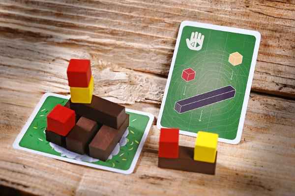 Brown wooden logs and red and yellow cubes stacked on green game cards over a textured wood surface.