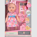 Blonde baby doll in a pink floral dress with bottle, dummy, and potty accessories inside a pink and grey window box.