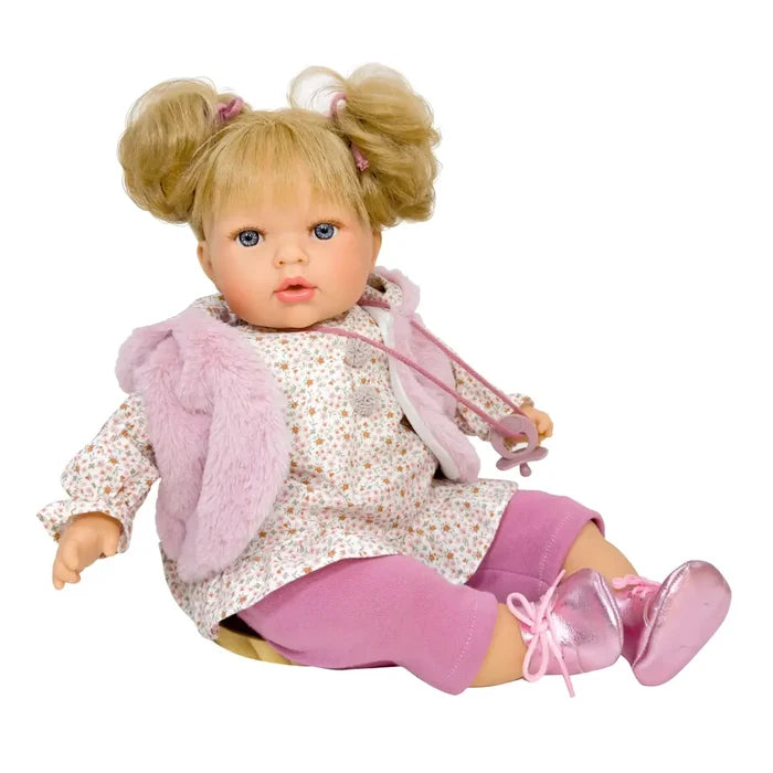 Blonde doll with pigtails wearing a pink faux-fur vest, floral dress, pink leggings, and metallic pink shoes.