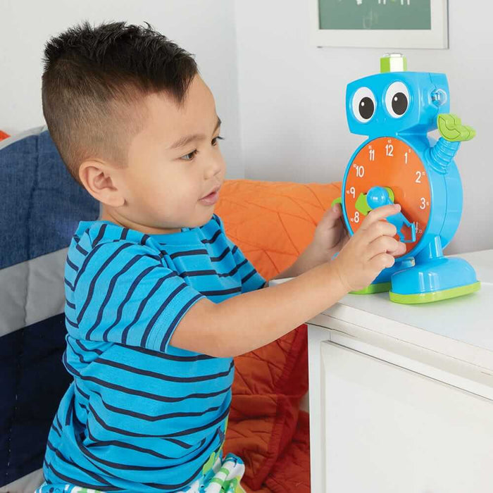 Young boy playing with a blue robot learning clock featuring an orange face, white numbers, and movable blue hands.