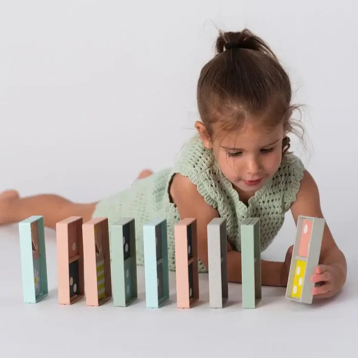 A child arranging large pastel-colored wooden domino blocks in pink, blue, and green on a white background.