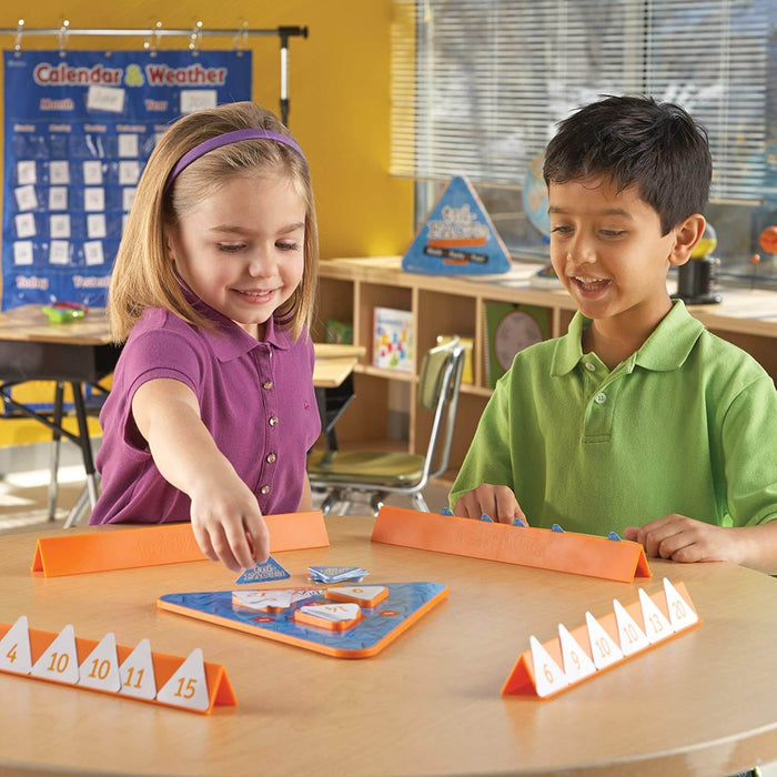 Two children play a math game with numbered triangular cards and orange holders at a table.
