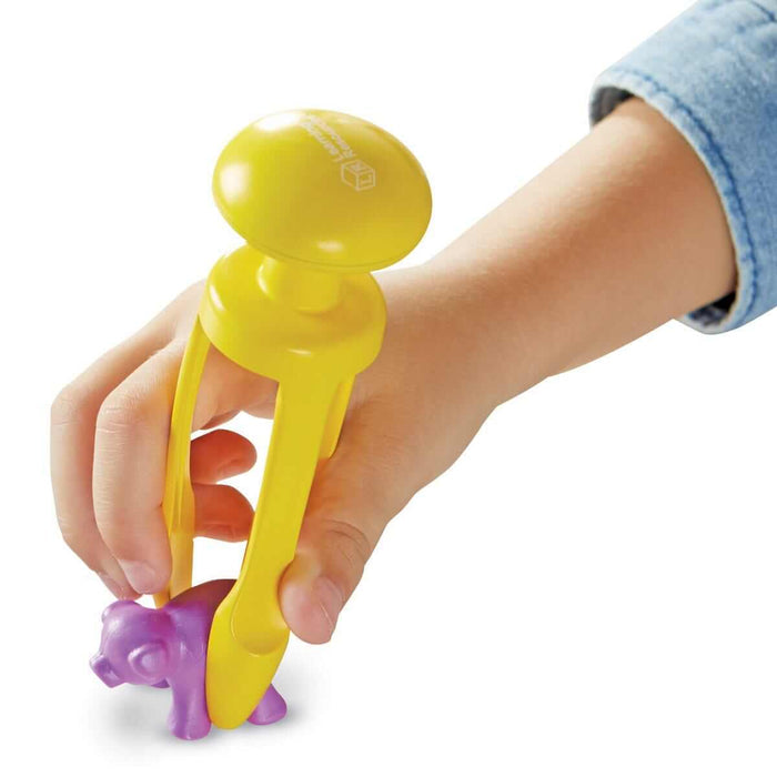 Child’s hand using yellow tongs with three prongs to pick up a small purple plastic animal toy.