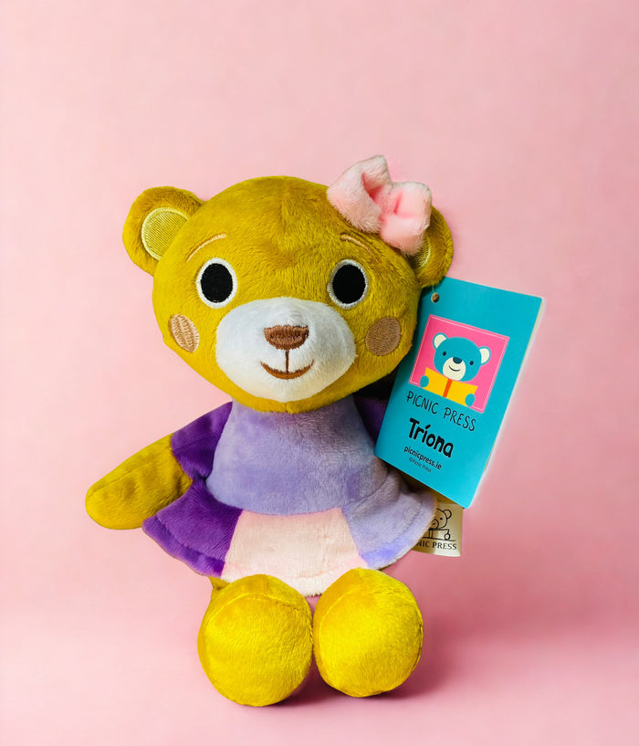 Yellow plush teddy bear wearing a purple and pink dress and pink ear bow, sitting against a pink background.