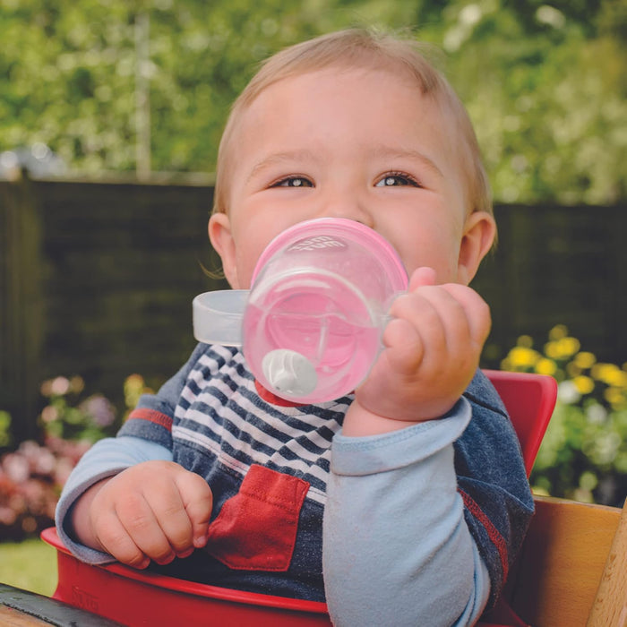 Baby in a red high chair drinking from a pink two-handle sippy cup with a weighted straw.