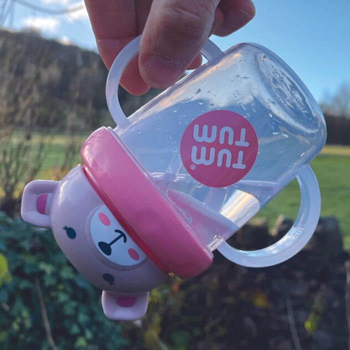 Upside-down clear training cup with white handles, a pink bear-shaped lid, and a weighted straw visible inside.