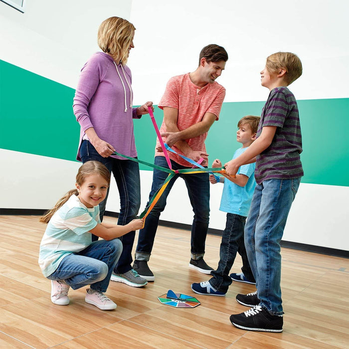 Family playing a game with colorful elastic straps joined at the center over a circular floor spinner.