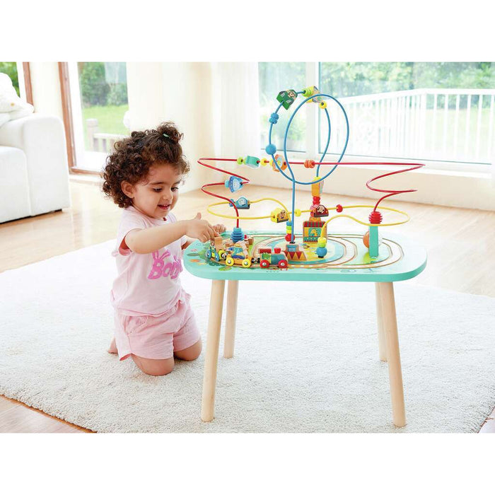 A young girl plays with a light blue activity table featuring a colorful wire bead maze and wooden train set.