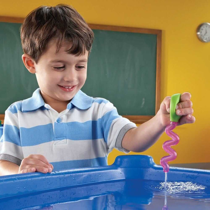 A child squeezes a pink spiral-shaped dropper with a green bulb to release water into a blue sensory table.
