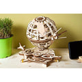 Intricate light wood mechanical 3D globe puzzle with gears and orbiting satellites next to a small green plant.