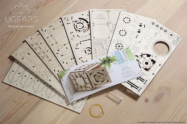 Fanned laser-cut wooden sheets, an instruction booklet showing a safe, toothpicks, and yellow rubber bands.