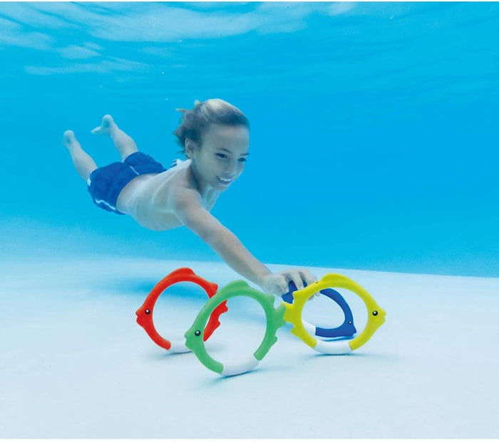 Child swimming underwater reaching for red, green, and yellow fish-shaped diving rings standing on the pool floor.