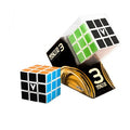 Two 3x3 V-Cubes with orange, blue, green, and black faces, one inside black and gold clear window packaging.