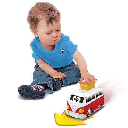 Toddler presses a yellow surfboard on a red and white cartoon VW van toy to make it zoom forward.