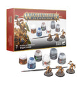 Retail box with six paint pots, a fine brush, and three gold fantasy warrior miniatures on textured grey bases.