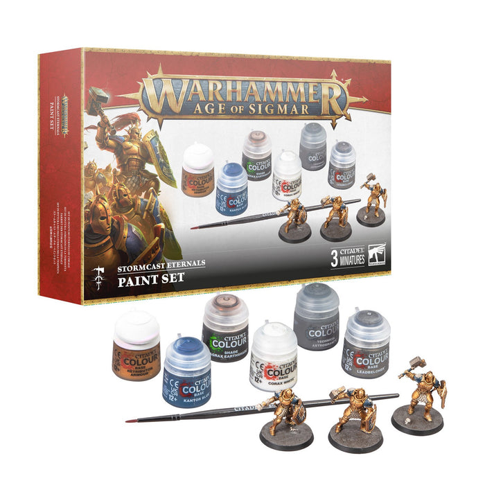 Retail box with six paint pots, a fine brush, and three gold fantasy warrior miniatures on textured grey bases.