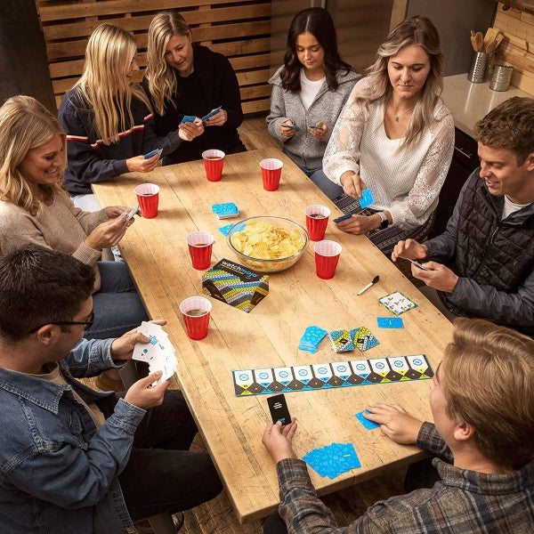 Six people play the WatchMojo party game with its yellow patterned box and blue cards on a light wooden table.