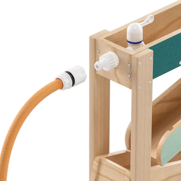 Close-up of an orange hose connecting to a wooden water track toy with white fittings and a manual tap handle.