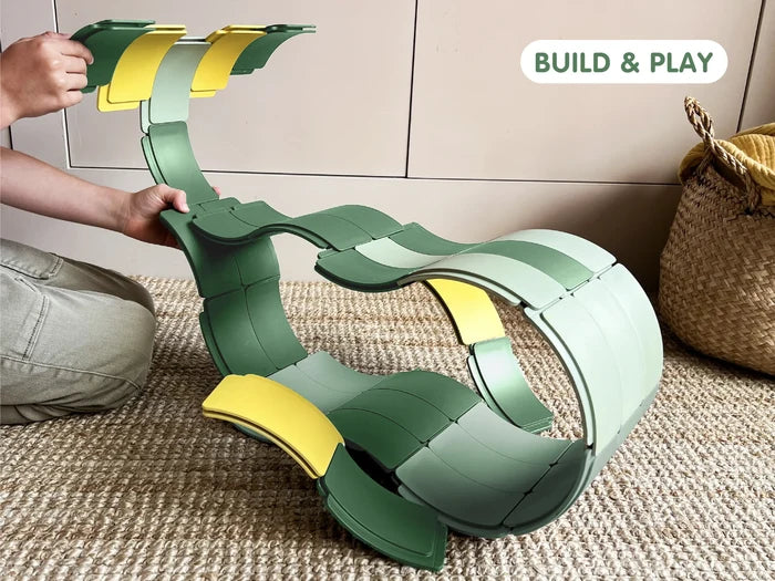 Child building a large wavy loop with shades of green and yellow curved interlocking pieces on a neutral rug.