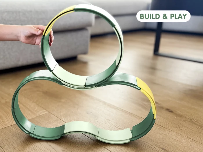 Child’s hand touching a stacked structure of green and yellow flexible track arches on a wood floor.