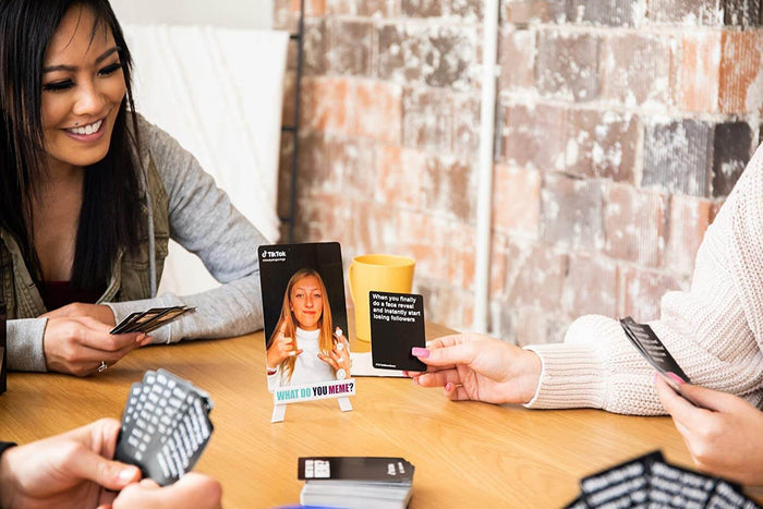 Friends play the What Do You Meme? TikTok Edition card game with viral photo cards and black text caption cards.