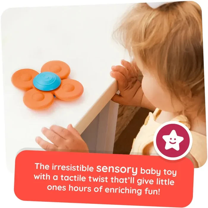 Toddler looking at a four-petaled orange and blue suction spinner toy on a white table.