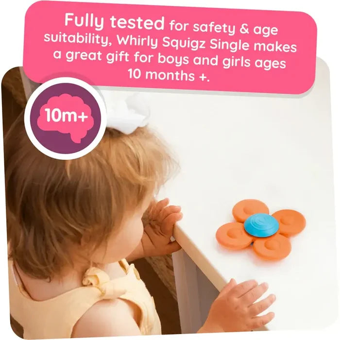 A toddler looks at an orange and blue flower-shaped suction toy stuck to a white tabletop.