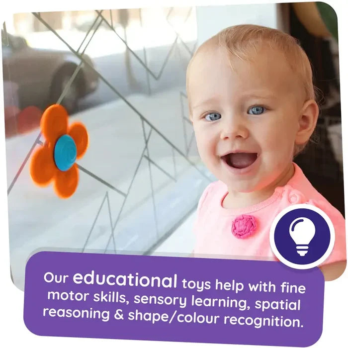 Smiling toddler next to an orange flower-shaped suction toy with a blue center stuck to a glass window.