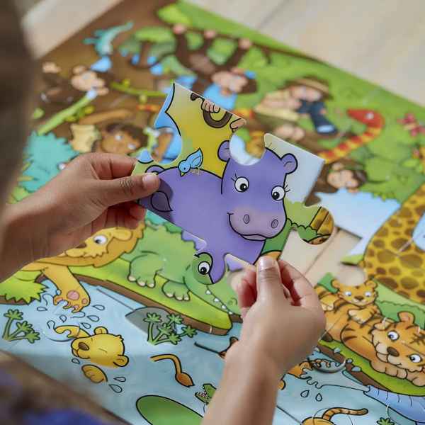Child's hands holding a large purple hippo piece over a colorful, illustrated jungle puzzle with lions and a crocodile.
