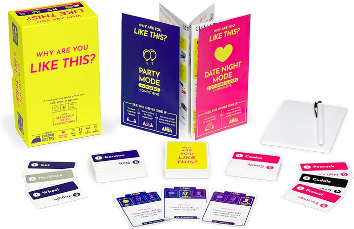 Yellow game box with pink text, blue and pink fold-out guides, several card decks, a white notepad, and a pen.