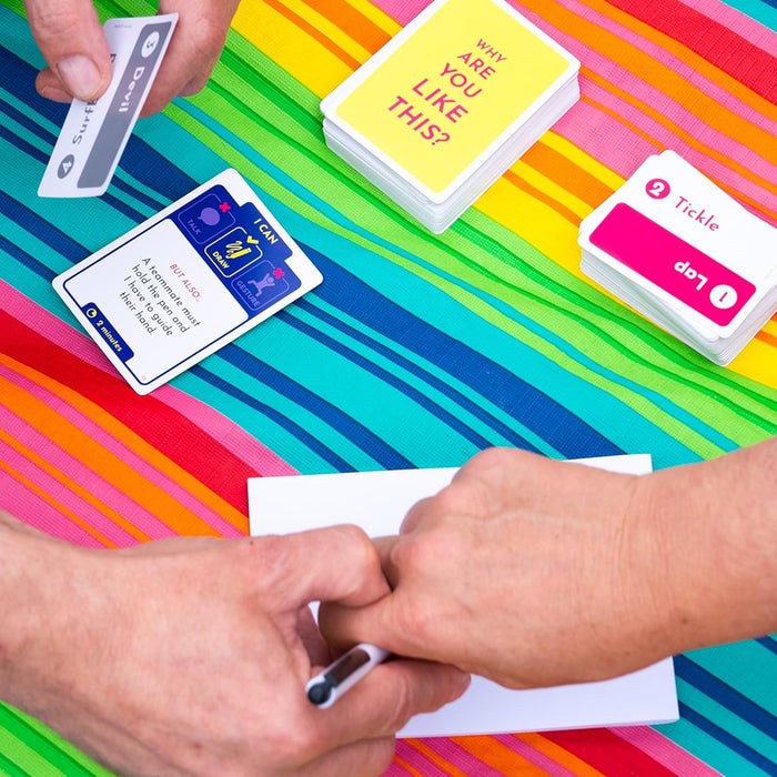 Hands guiding a pen over paper, surrounded by colorful game cards on a vibrant rainbow-striped background.