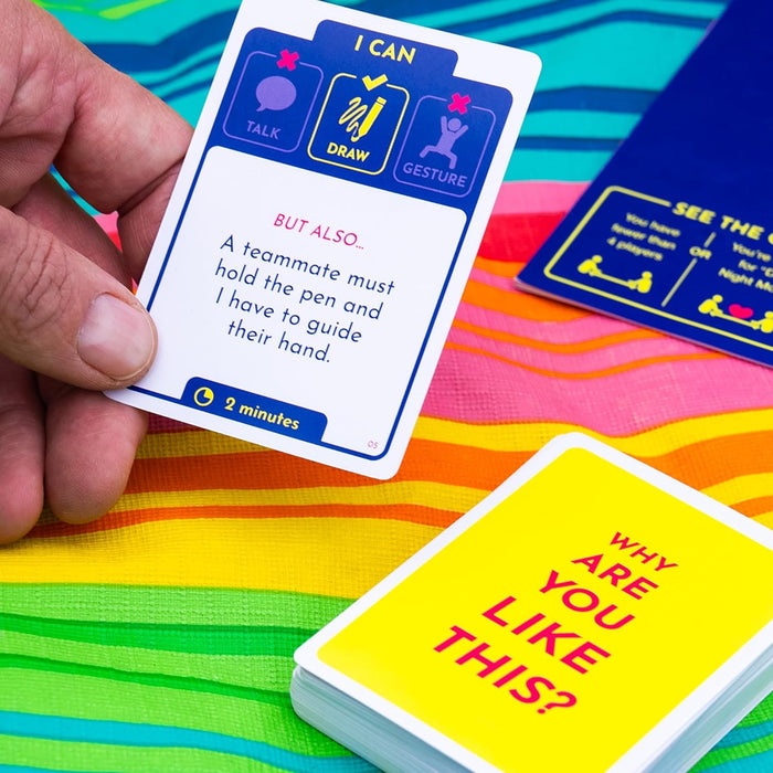 Hand holding a game card with instructions over a yellow deck of cards on a vibrant, multi-colored striped surface.