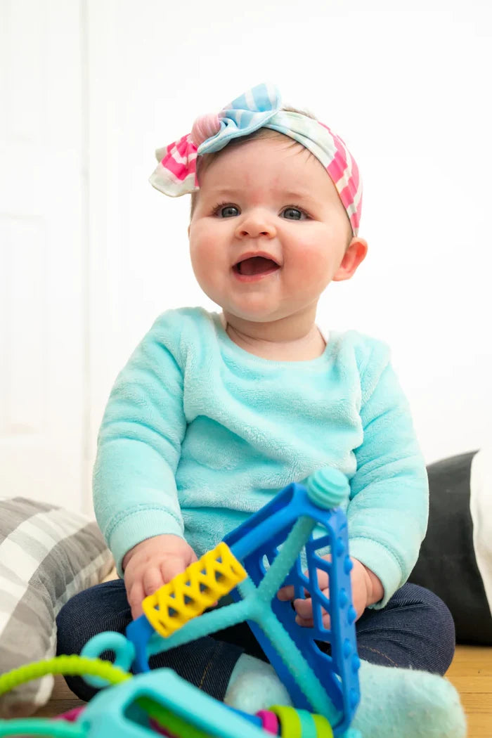 Smiling baby in a blue fuzzy sweater playing with a blue triangular toy with yellow rungs and colorful textures.
