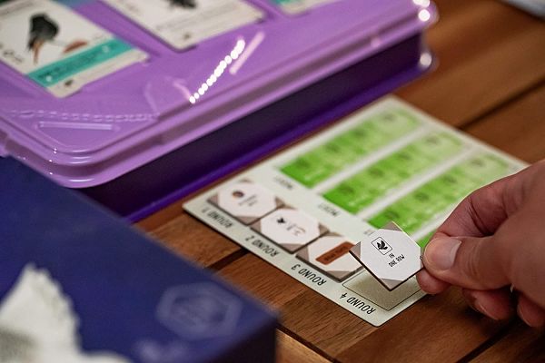 Hand placing a goal tile on a scoring board next to a purple card tray and green bird cards.