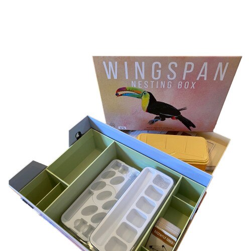 Open game organizer box with toucan lid art, green interior dividers, and white and yellow plastic sorting trays.