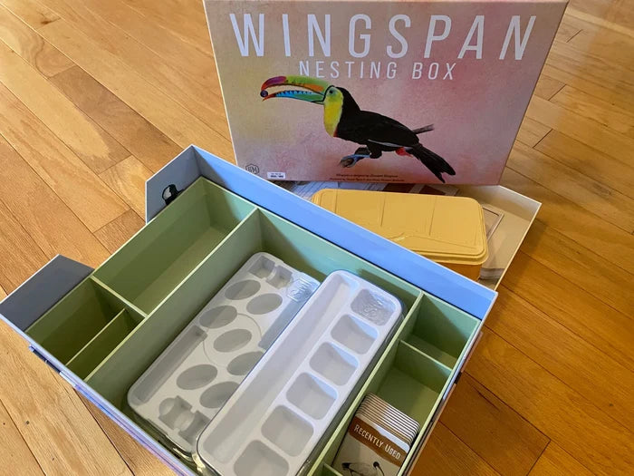 Open storage box with green dividers and plastic trays, featuring a lid with a colorful toucan illustration.