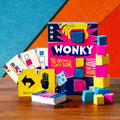 Bright blue and pink game box with a tower of colorful cubes and playing cards on a wooden table.