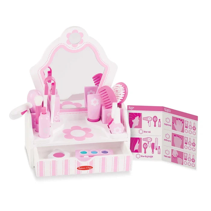 Pink and white wooden toy vanity with mirror, open drawer, and beauty tools like a hairdryer, brush, and nail polish.